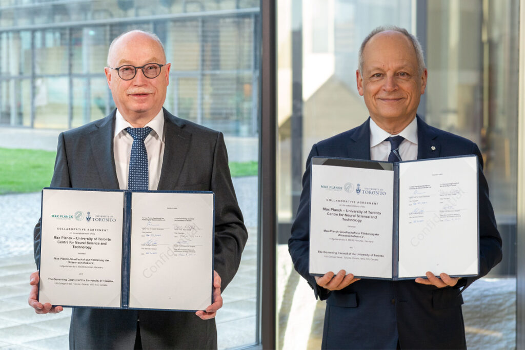 Side-by-side images of Meric Gertler and Martin Stratmann. Each man smiles and holds up a signed document.