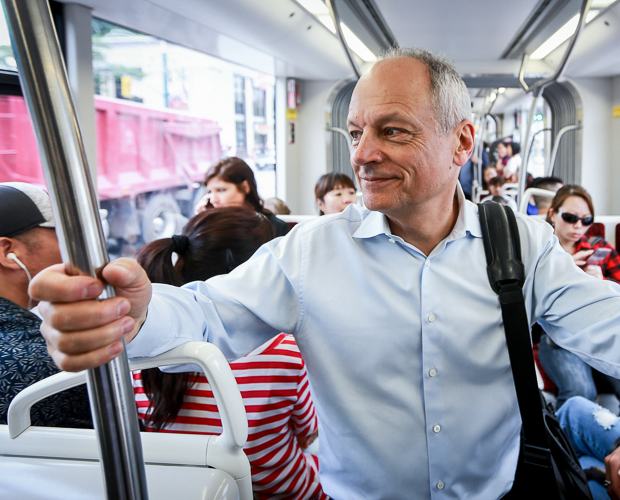 Meric Gertler smiles as he stands in a street car in Toronto, holding on to a pole.