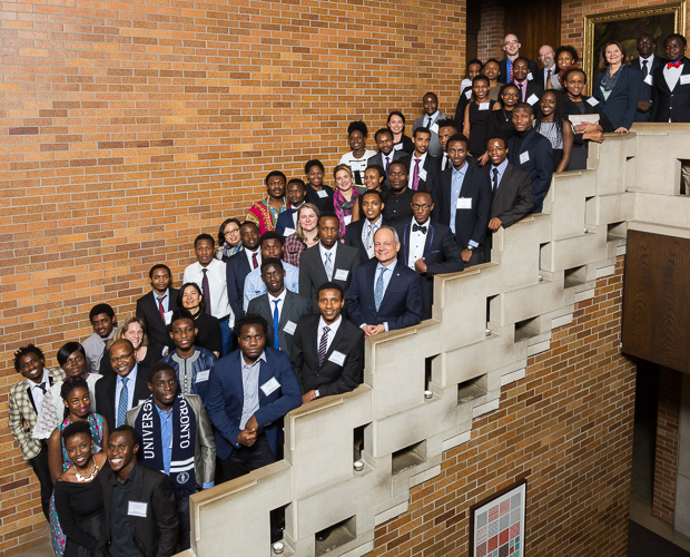 More than 50 Mastercard scholars stand on a staircase for a group photo with Meric Gertler. Everyone is smiling.